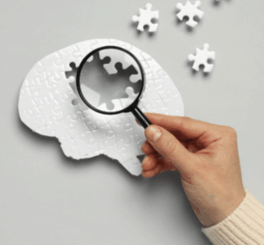 Puzzle in the shape of a brain with a hand using a magnifying glass to find the missing pieces